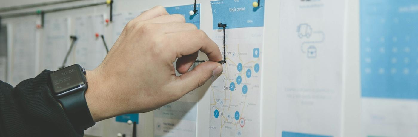 Hand ordnet ausgedruckte UI-Entwürfe an einer Wand